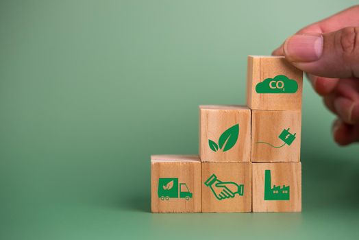 Hand holding wood cube block icon co2 carbon credit and eco energy green technology on green background.