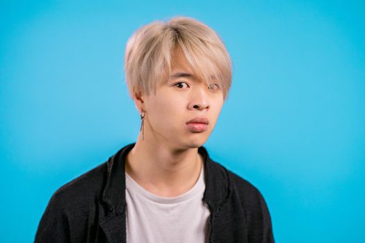 Asian furious man on blue background. Korean guy in stress and rage, he is in aggression and looking at camera with disgust