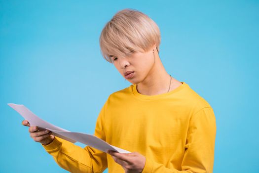 Young asian man checks documents, utility bills, report. Guy isolated on yellow background.