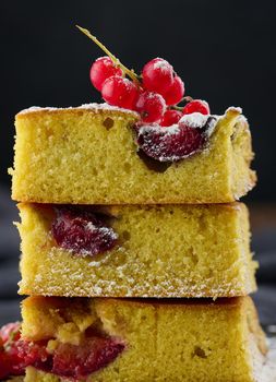 A stack of square slices of baked plum biscuit cake, sprinkled with powdered sugar on top