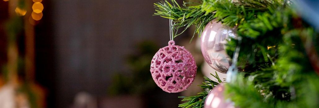Silver and pink bauble hanging on a decorated snow tree. Christmas holiday background.Christmas toy ball. New year tree decorated with a garland.Concept Of A Happy winter holidays.web banner