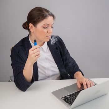 Business woman smoking a disposable vape while sitting at her desk.
