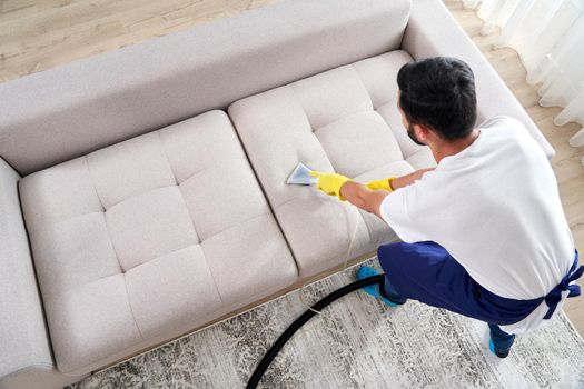 Close-up of housekeeper holding modern washing vacuum cleaner and cleaning dirty sofa with professionally detergent. Professional springclean at home concept