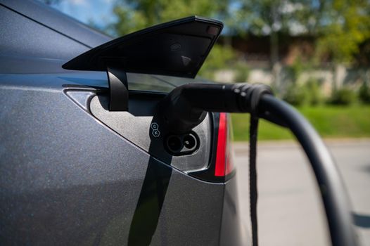 Black electric car charging outdoors in summer.