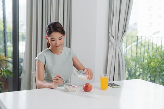 Woman pouring milk on plate with cereal muslin at kitchen