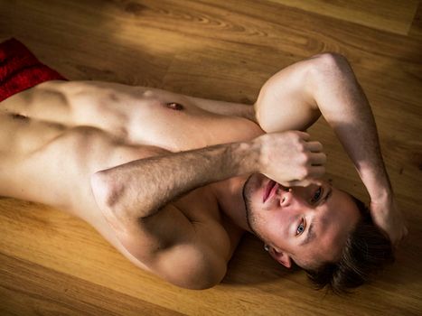Totally naked muscular young man laying on floor