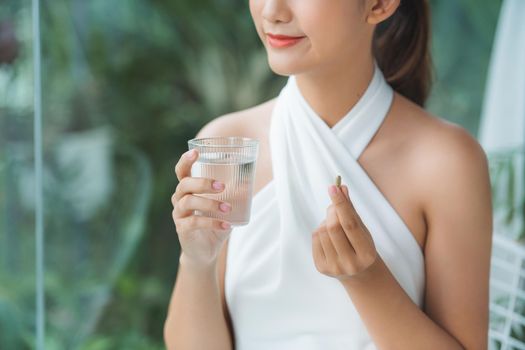 Millennial pretty asian female hold pill and glass of water 
