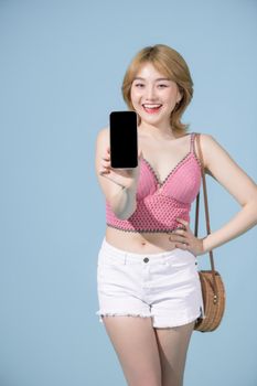 Happy asian woman holding and showing innovative smartphone laughing at camera on blue background