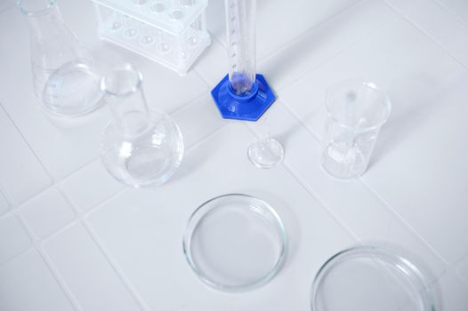 Overhead view of labware for biochemical experiment. Petri dish, flasks, graduated cylinder, beaker on a white table