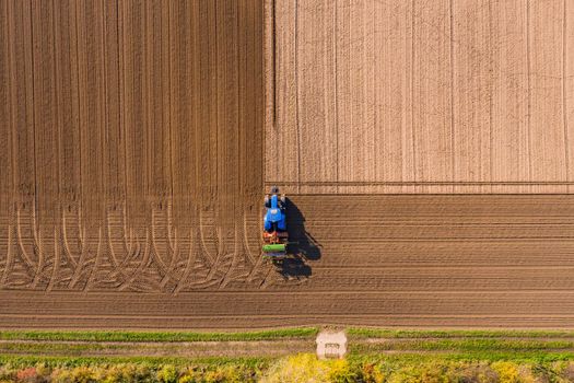 Aerial view of blue tractor plowing a field leaving tire tracks