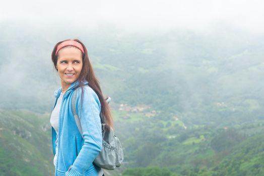 Smiling female traveler against foggy mountain landscape