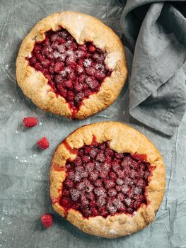 Two perfect raspberry galettes. Delicious rustic homemade tart with frozen or fresh raspberries, gray background. Beautiful round galettes with raspberries, copy space. Vertical. Top view or flat lay