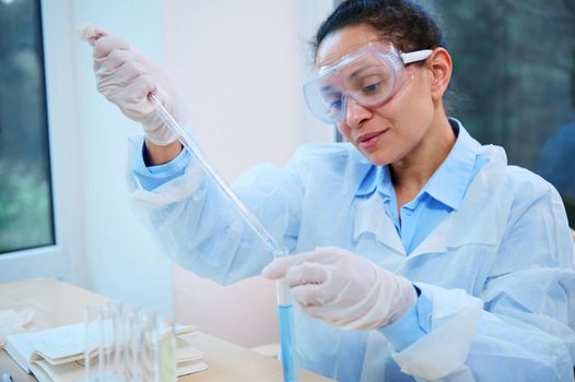 Latin American pharmacologist uses a graduated glass pipette, drips a substance into a test tube in science laboratory
