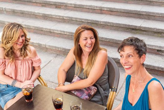 Three adult women in a cafe outside laughing and having drinks