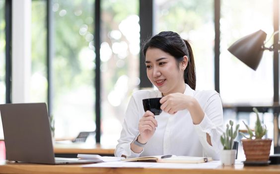 Young asian businesswoman have the pleasure of watching work on their laptop and favorite coffee at the office.