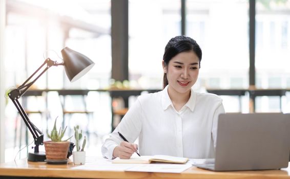 Beautiful young asian woman sitting at coffee shop using laptop. Happy young businesswoman sitting at table in cafe with tab top computer.