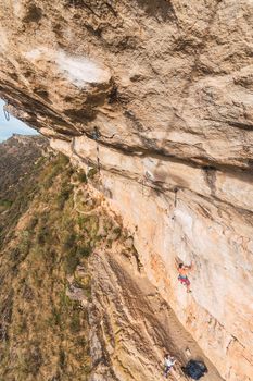Aerial view of a rock climber climbing a rock formation with people watching from the ground