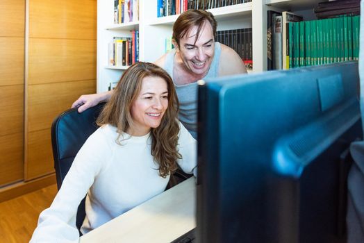 Middle-aged couple looking happy at computer at home