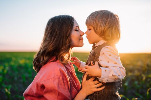 Tender scene of loving son with mom on sunset backdrop. Beautiful family. Cute 3 year old kid with mother. Parenthood, childhood, happiness, children wellbeing concept.