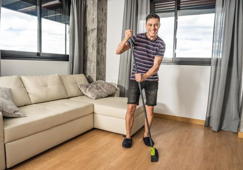 Smiling man sweeping his living room. Household chores concept.