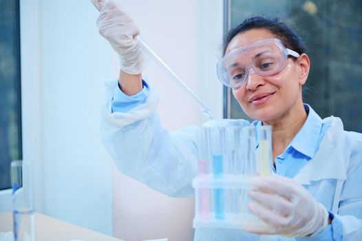 Inspired Hispanic woman lab assistant, scientist chemist using lab dropper dripping few chemical reagent into test tubes