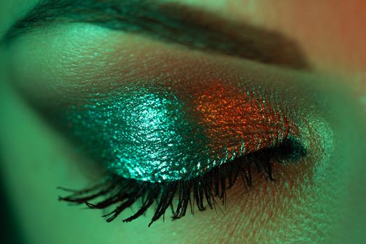 Extreme close up of female eye iris under neon light. Woman with beautiful makeup, glitter shadows and false lashes. Girls green eye. Nightlife, night club concept.