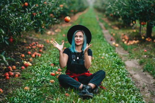 Blue haired woman picking up ripe red apple fruits in green garden. Organic lifestyle, agriculture, gardener occupation