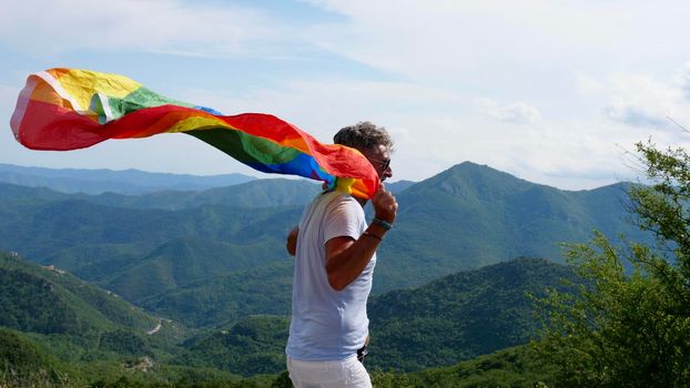 Old gay man walks with LGBT rainbow flag