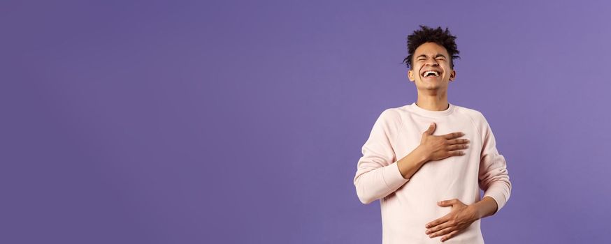 Portrait of cheerful, happy young hipster guy laughing out loud from hilarious joke, watching awesome stand-up performer, chuckle and touchign chest, bending backwards from laugh