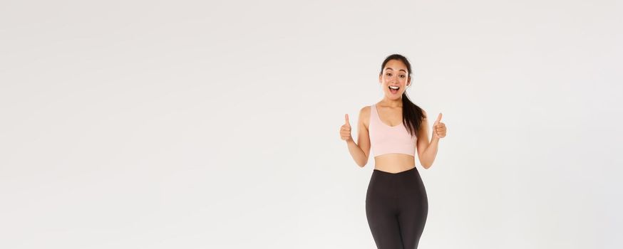 Full length of amazed and satisfied smiling fitness girl, female athelte in active wear liking new gym or workout program, showing thumbs-up pleased, encourage start training or doing exercises