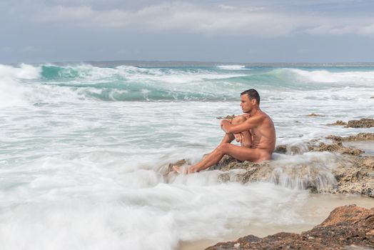 Tranquil nude man sitting on beach near sea