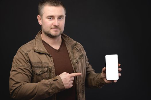 Mature middle-aged man in casual clothes presenting an application on a smartphone while holding in his hand showing a cut-out mockup screen. studio portrait