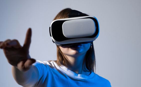 Young brunette woman in white t-shirt wearing virtual reality headset touching air during the VR on Metaverse experience. Metaverse technology concept.