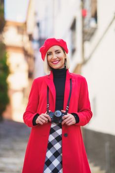 Content stylish lady with camera on neck smiling on town street