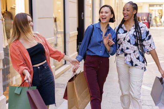 Cheerful diverse women with shopping bags meeting on street