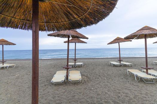 Empty beach with sun loungers and umbrellas in the early morning and a cloudy sky. Crete Greece.
