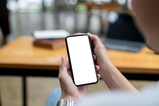 Mockup image of a woman holding black mobile phone with blank white screen while sitting in cafe.