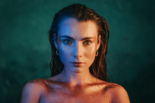 Portrait of young beautiful model girl with original golden make-up and sparkles on blue background.Concept of haute couture, art visage, femininity.
