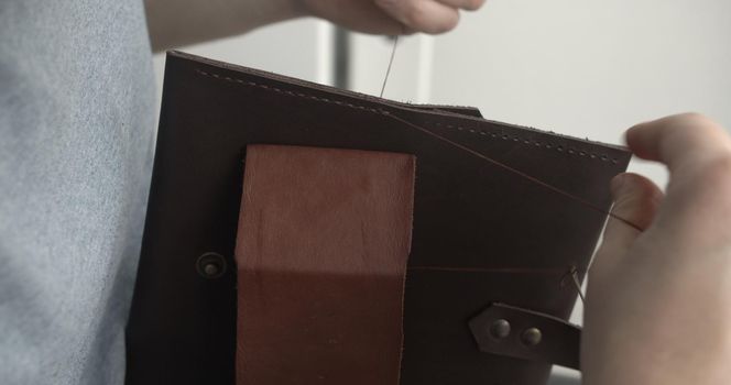Making a handmade brown leather wallets. The hands of the master sew a leather product.