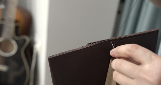 Sewing a brown leather wallet. Leather work. Sewing products by hand. Manufacture of leather goods.