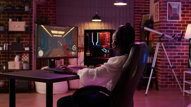 Over shoulder view of african american gamer girl using pc gaming setup playing multiplayer streaming online action game