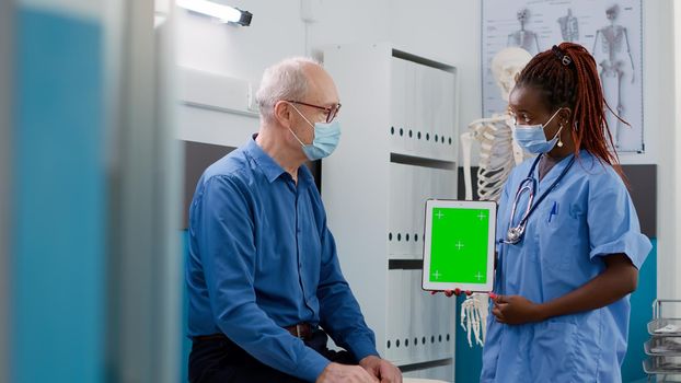 Assistant showing tablet with greenscreen to senior patient