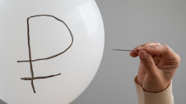 Caucasian woman pops a balloon with a ruble inscription with a needle.