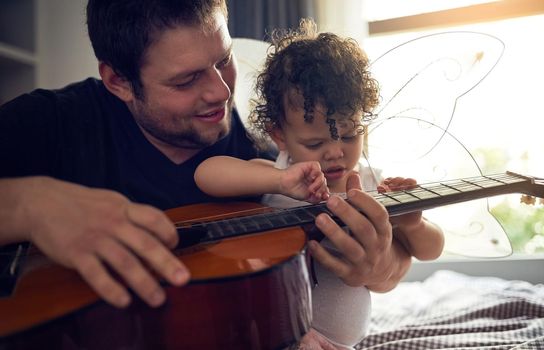 Music runs in the family. a father teaching his baby daughter all about the guitar.