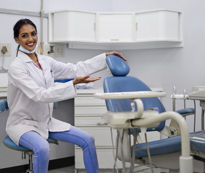 Lets get your dental health in check. Portrait of a young female dentist gesturing to sit in the dental chair in her office