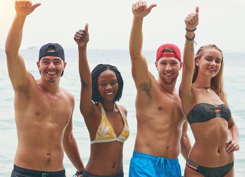 This holiday gets our vote. Portrait of a group of happy tourists showing thumbs up while posing by the ocean.