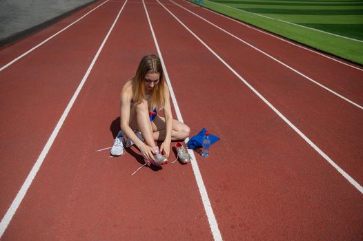 Young caucasian woman tying shoelace before jogging at stadium.