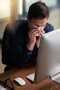 The flu has really gotten to him. a young businessman blowing his nose in an office.