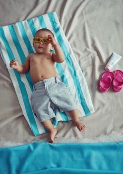 I was born for the beach life. Concept shot of an adorable baby boy lying on a towel at a make believe beach.