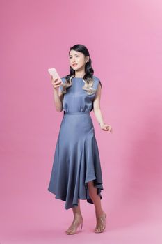 Full length young asian woman with hold mobile cell phone chat online walk go isolated on pink background